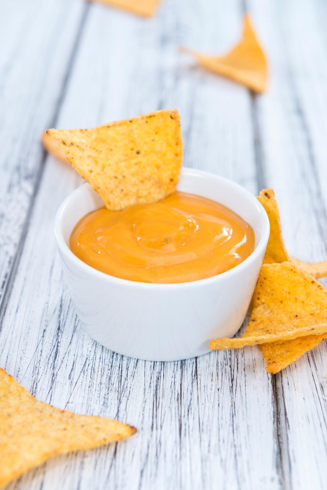 Nachos with Cheese Dip (close-up shot) on an wooden table