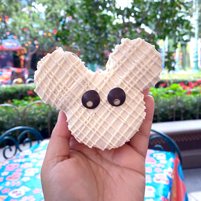 A macaron in the shape of mickey's head, covered in vanilla frosting that's strung across to look like mummy bandages