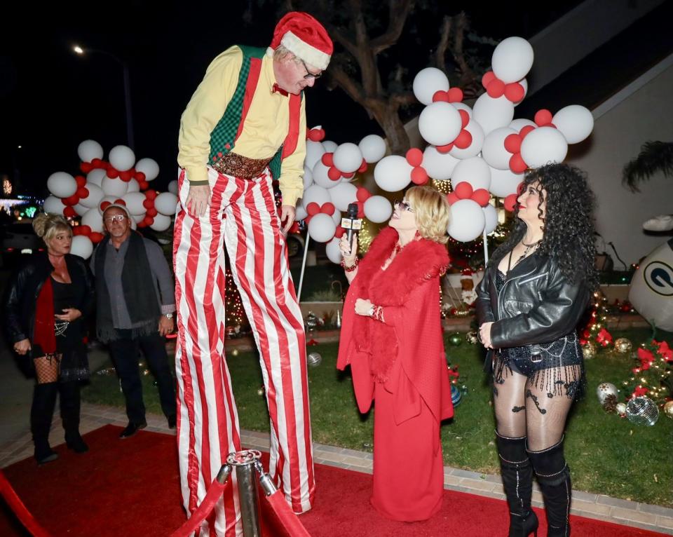 A Joan Rivers impersonator interviews a performer on stilts while 