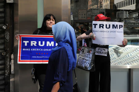 A woman wearing a Muslim headscarf walks past people holding U.S. Republican presidential nominee Donald Trump signs before the start of the annual Muslim Day Parade in the Manhattan borough of New York City, September 25, 2016. REUTERS/Stephanie Keith/Files