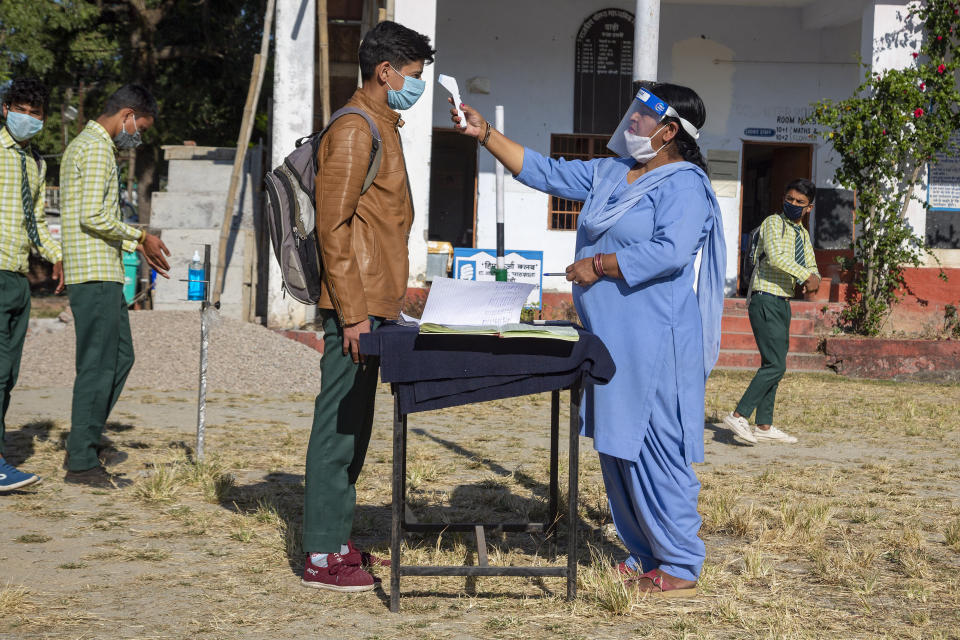 A staff member tests the temperature of students before allowing them into classrooms, as a precautionary measure against the coronavirus, at the Government Senior Secondary School in Dari, near Dharmsala, India, Friday, Nov. 6, 2020. (AP Photo/Ashwini Bhatia)