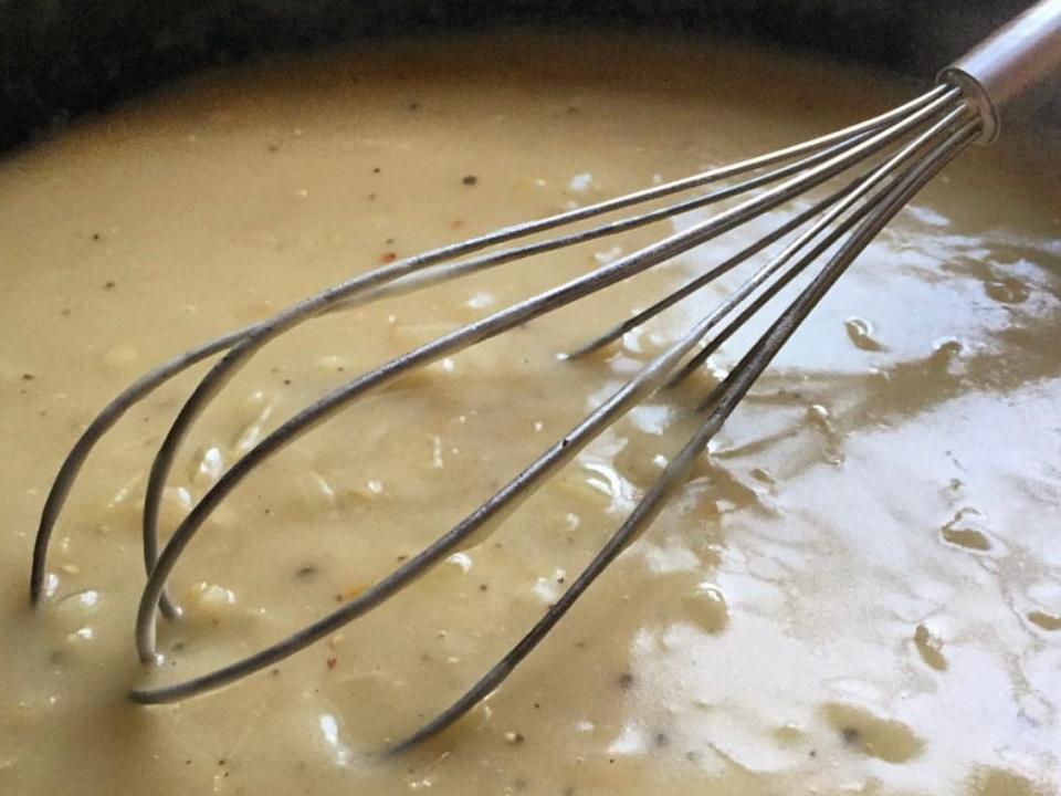 A whisk in a pool of light-colored gravy