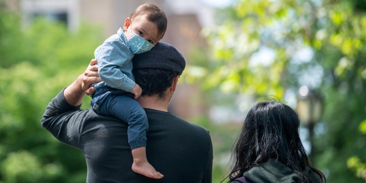 A youngster wearing a mask looks at the camera while sitting on his father's shoulder in Central Park on May 24, 2020 in New York City.
