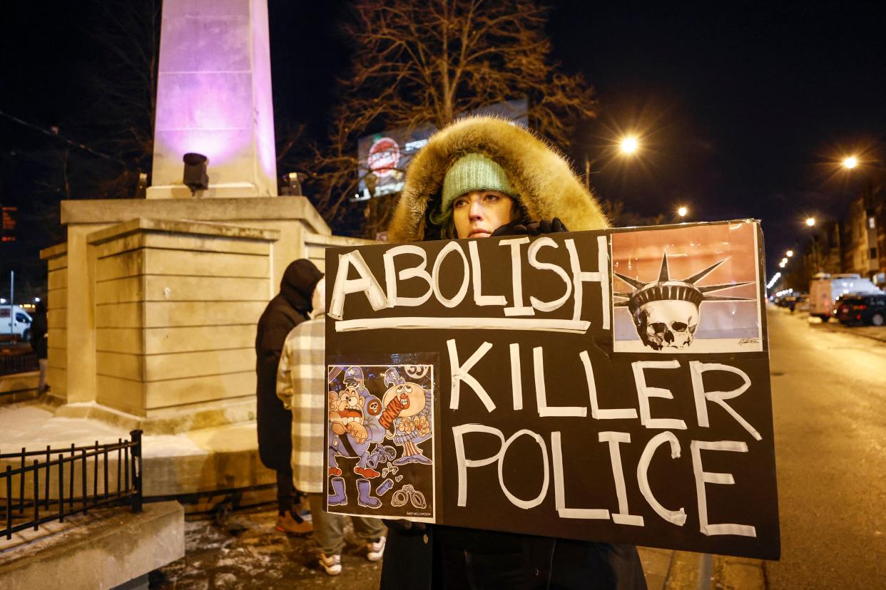 A protester holds a sign reading: Abolish Killer Police, showing the head of the Statue of Liberty as a skull and a caricature of a police officer jumping out of his boots and dropping his truncheon as a figure shouts Honk behind him.