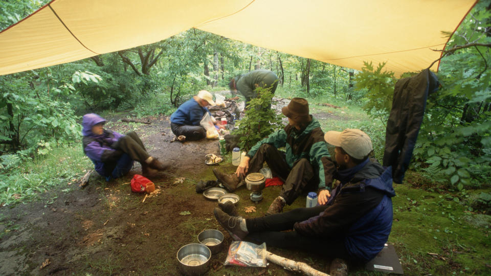 A group of campers hang out under a tarp