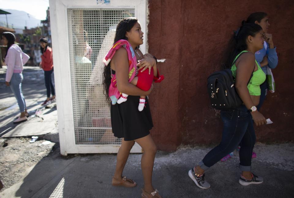 In this photo taken July 25, 2019, 15-year-old Nicol Ramirez carries her baby girl into a clinic where she hopes to get a hormonal implant to prevent future pregnancies in the Caucaguita neighborhood on the outskirts of Caracas, Venezuela. Ramírez and her sister were among the lucky few to get the last of the implants after their mom paid for a pregnancy test and they were able to prove they were not pregnant. (AP Photo/Ariana Cubillos)