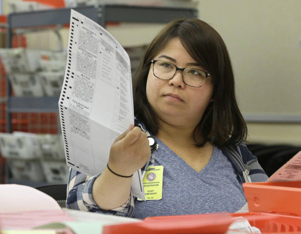 FILE - In this June 10, 2016 file photo, San Li, a temporary worker at the Sacramento County Registrar of Voters office, inspects a mail-in ballot before it is counted in Sacramento, Calif. Winners in close U.S. House races from the Nov. 6, 2018 election might not be known for days or weeks in Washington state and California. (AP Photo/Rich Pedroncelli, File)
