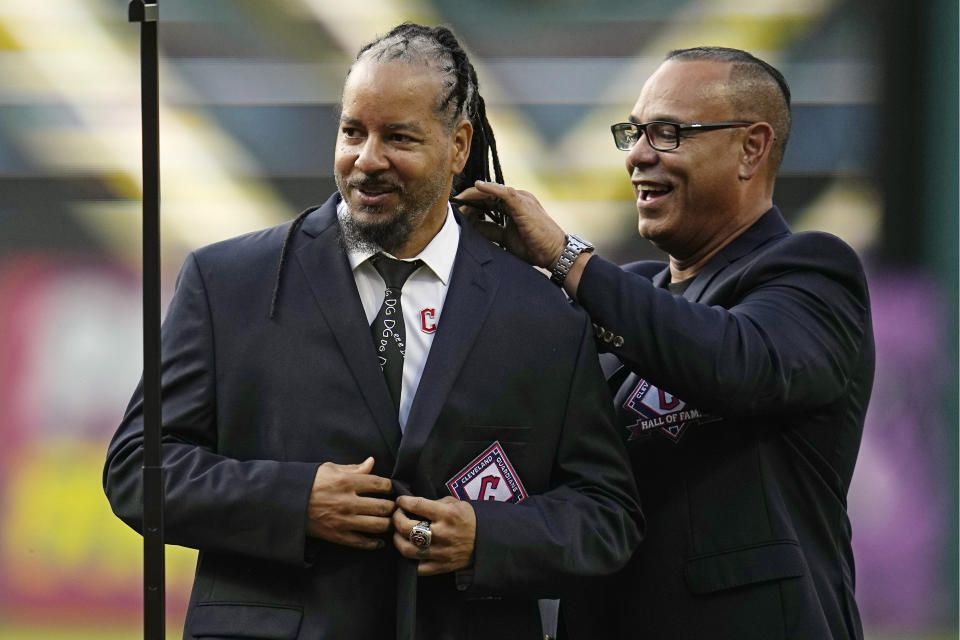 Former Cleveland baseball player Manny Ramirez, left, is helped into his Hall of Fame jacket by former teammate Carlos Baerga, right, during induction ceremonies into the Cleveland Guardians Hall of Fame before a game between the Detroit Tigers and the Guardians, Saturday, Aug. 19, 2023, in Cleveland. (AP Photo/Sue Ogrocki)