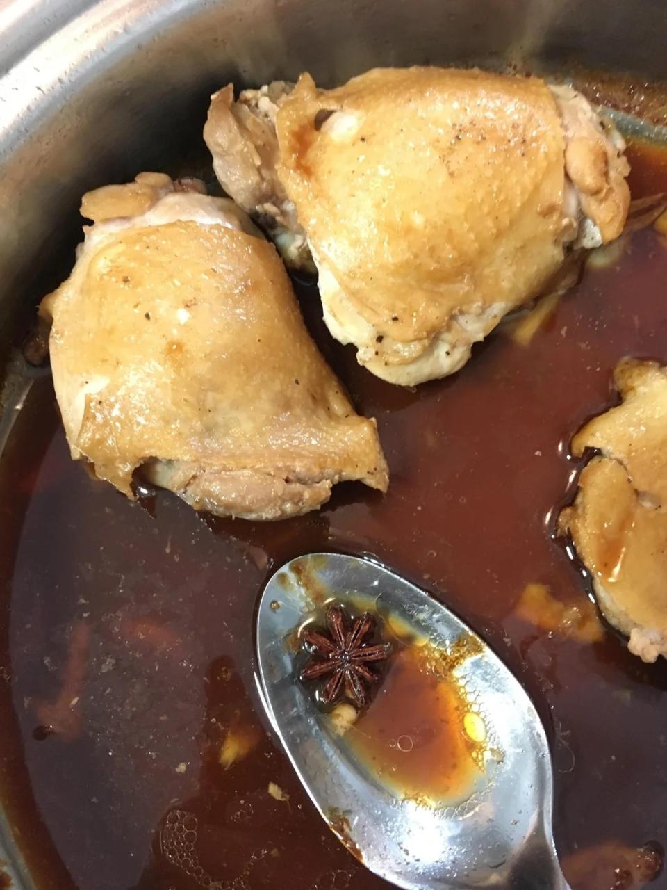 A pot with three cooked chicken thighs in a brown sauce, with a spoon holding a star anise