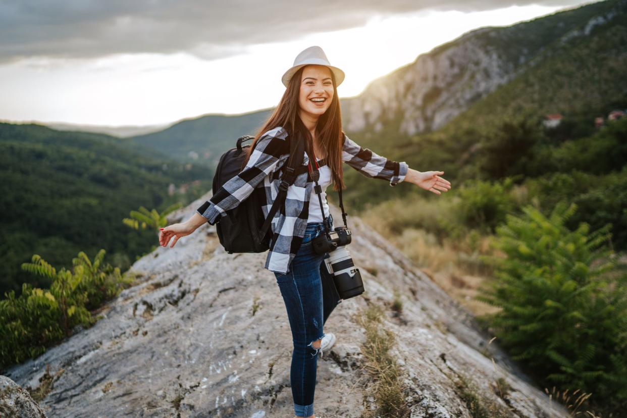 Happy young traveler woman with backpack and camera on mountain rock