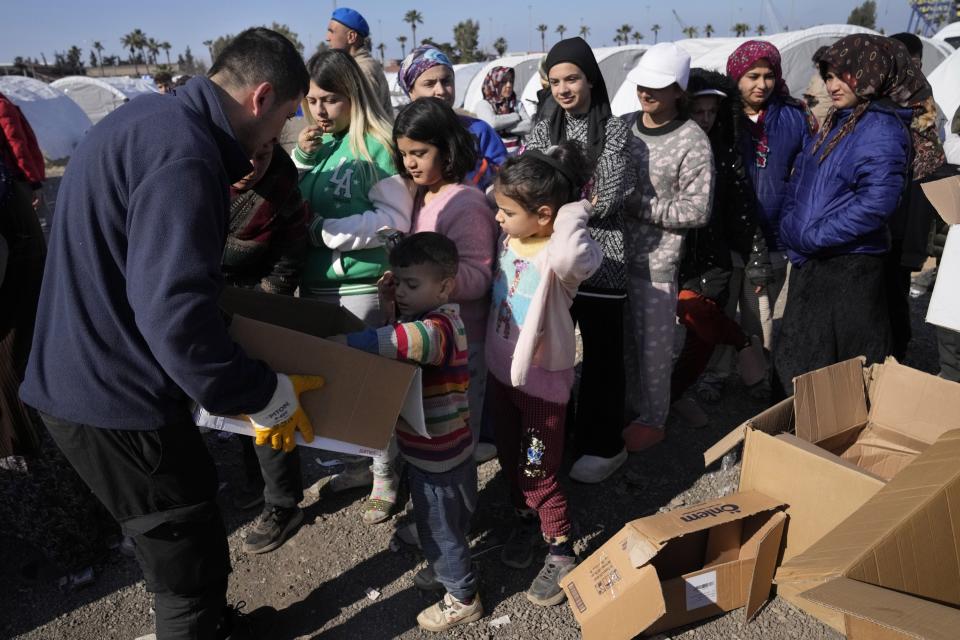 A volunteer, left, distributes food for people who lost their houses in the devastating earthquake, as they lineup with boxes to receive aid supplies at a makeshift camp, in Iskenderun city, southern Turkey, Tuesday, Feb. 14, 2023. Thousands left homeless by a massive earthquake that struck Turkey and Syria a week ago packed into crowded tents or lined up in the streets for hot meals as the desperate search for survivors entered what was likely its last hours. (AP Photo/Hussein Malla)