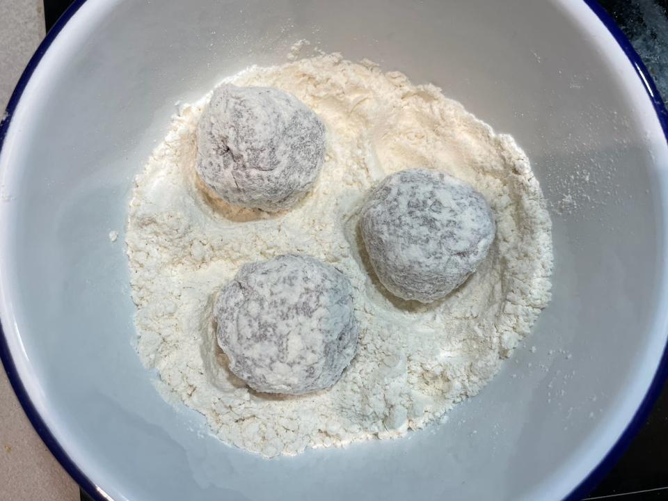 three meatballs covered in flour in a ceramic bowl of flour