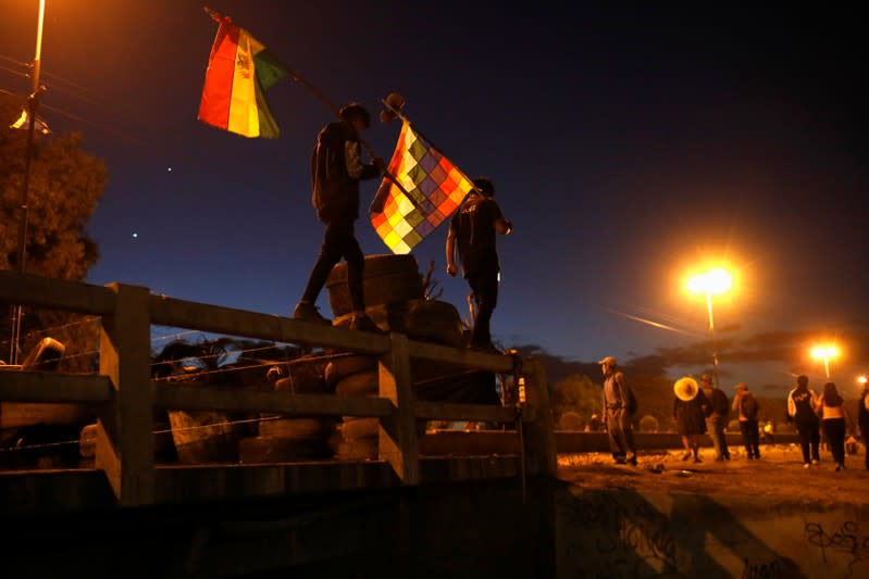 Men wave Bolivian and Wiphala flags as coca farmers and supporters of Bolivia's ousted President Evo Morales stage a blockade of an entrance to Sacaba