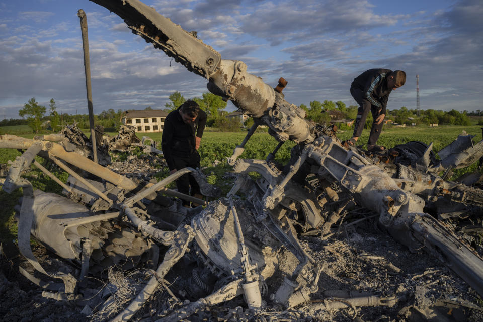 Oleksiy Polyakov, right, and Roman Voitko check the remains of a destroyed Russian helicopter lie in a field in the village of Malaya Rohan, Kharkiv region, Ukraine, Monday, May 16, 2022. (AP Photo/Bernat Armangue)