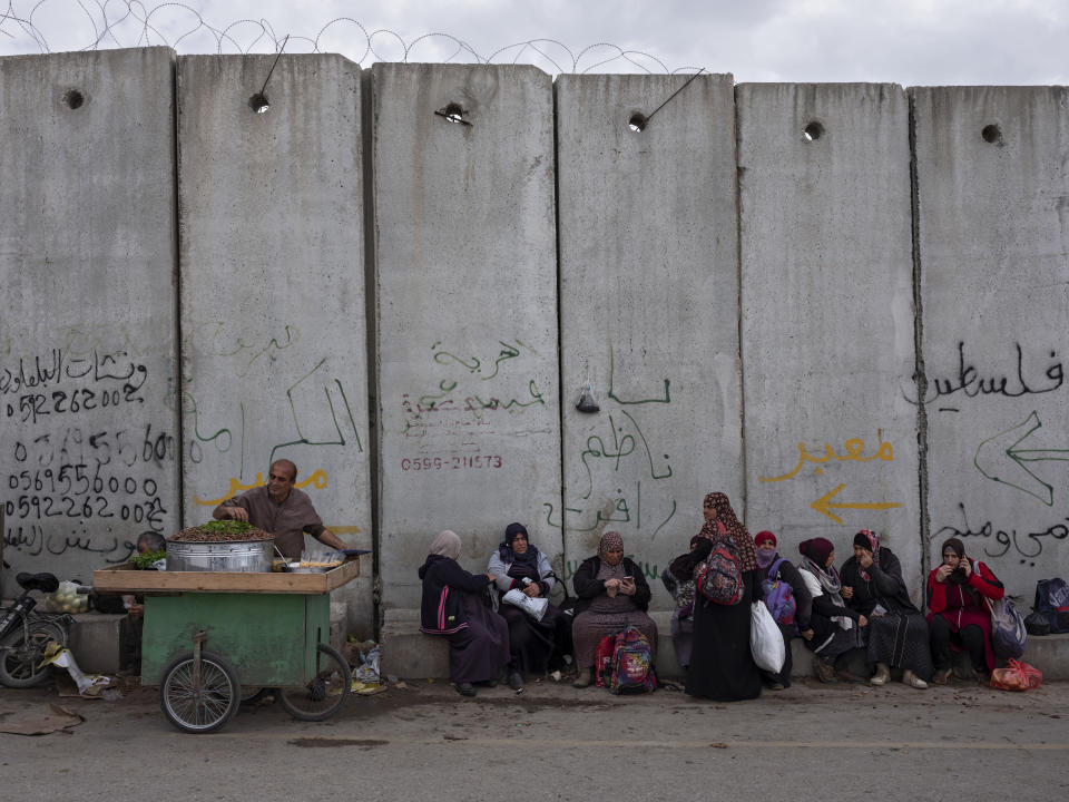 FILE - Palestinian women sit on a section of Israel's concrete separation barrier next to a small market at the West Bank city of Qalqilya, March 9, 2022. (AP Photo/Oded Balilty, File)