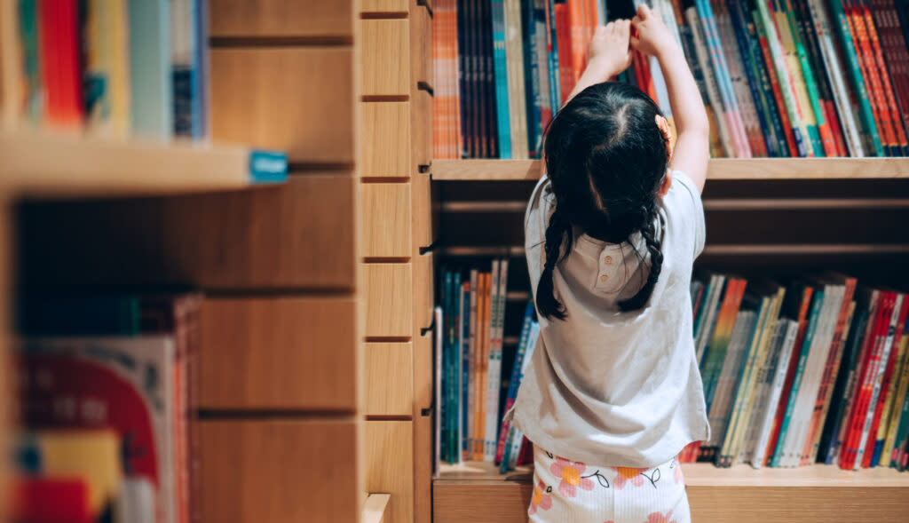 Little girl choosing books from the bookshelf in library