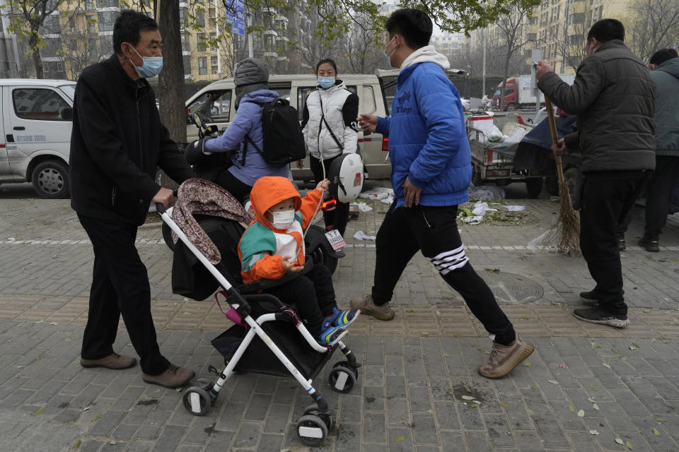 A child wearing a mask is pushed in his stroller in Beijing, Thursday, Nov. 24, 2022. China is expanding lockdowns, including in a central city where factory workers clashed this week with police, as its number of COVID-19 cases hit a daily record. (AP Photo/Ng Han Guan)