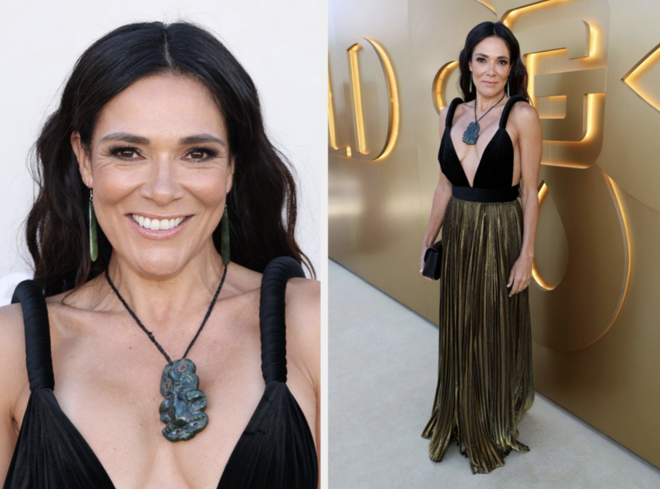 Simone Kessell at an event, wearing a black top with a deep neckline and a gold pleated skirt, smiling at the camera