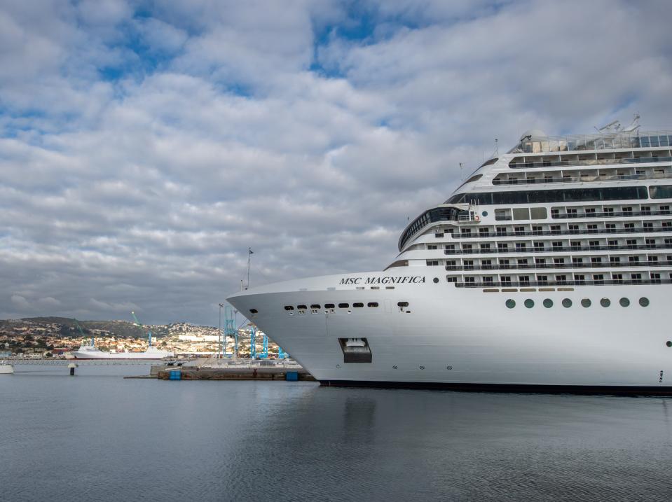 The MSC Magnifica is docked at the cruise terminal of the Port of Marseille in France in 2023. There are cloudy blue skies in the background.