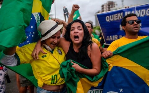 Supporters of Brazilian presidential candidate for the Social Liberal Party (PSL) Jair Bolsonaro cheer in front of the residential condominium where he lives, in Barra da Tijuca - Credit: AFP