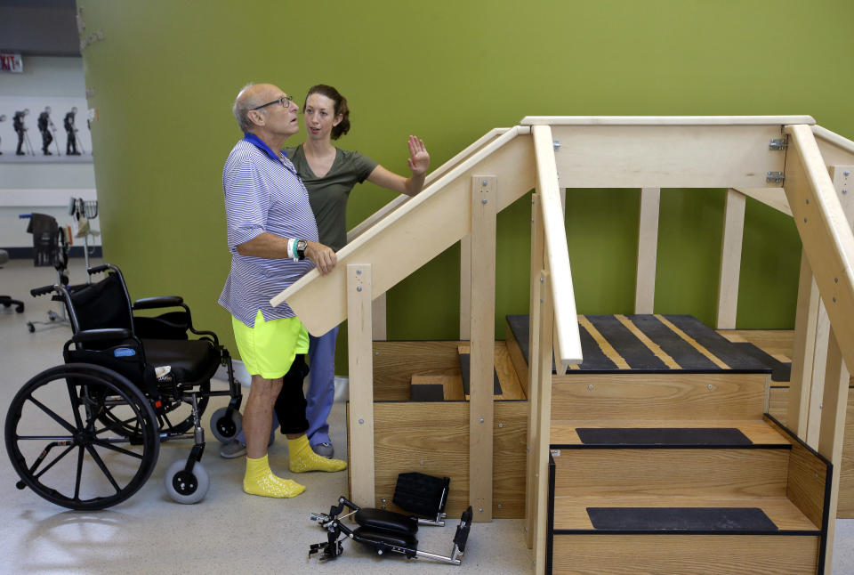 William Lytton, of Scarsdale, N.Y., left, is assisted by physical therapist Caitlin Geary, right, as he prepares to climb a set of stairs at Spaulding Rehabilitation Hospital, in Boston, Tuesday, Aug. 28, 2018, while recovering from a shark attack. Lytton suffered deep puncture wounds to his leg and torso after being attacked by a shark on Aug. 15, 2018 while swimming off a beach, in Truro, Mass. Lytton injured a tendon in his arm while fighting off the shark. (AP Photo/Steven Senne)