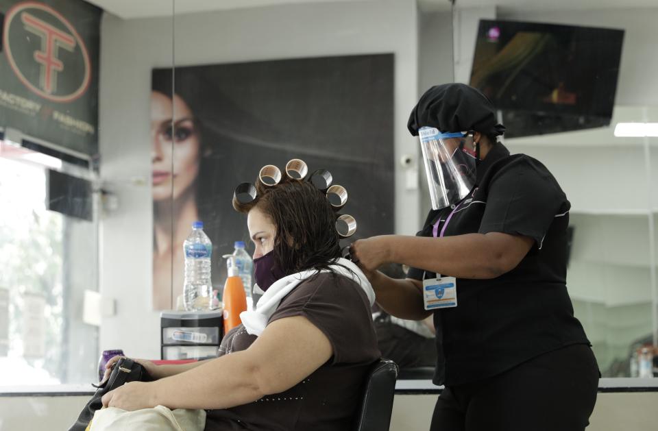 A hairstylist services a client at the Factory Fashion Beauty Salon in Panama City, Monday, Aug. 17, 2020. After nearly five months of quarantine, on Monday Panama is starting a partial reopening of the economy, with barbers, beauty salons, retail, and car lots opening their doors, in an effort to revive the economy while preparing for another possible spike in coronavirus cases. (AP Photo/Arnulfo Franco)