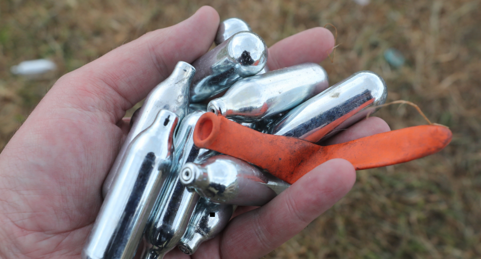 Image of nitrous oxide canisters, known as 'nangs', and a balloon all found on the ground. 