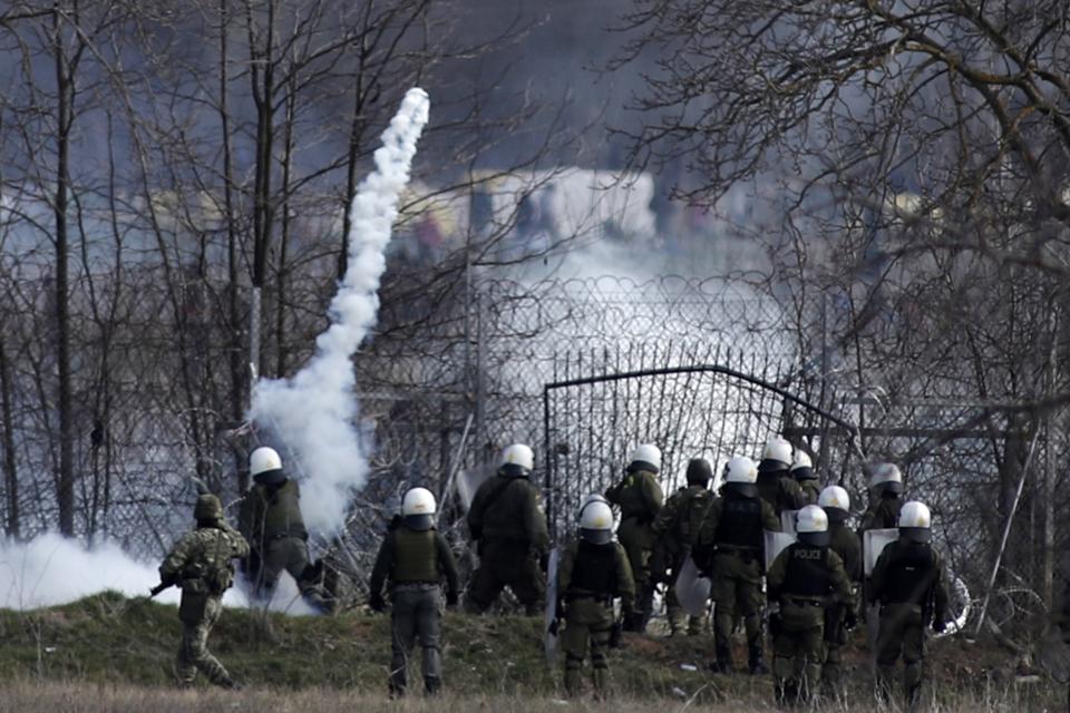 Greek police guard as migrants gather at a border fence on the Turkish side, during clashes at the Greek-Turkish border in Kastanies, Evros region, on Saturday, March 7, 2020. Thousands of refugees and other migrants have been trying to get into EU member Greece in the past week after Turkey declared that its previously guarded borders with Europe were open. (AP Photo/Giannis Papanikos)