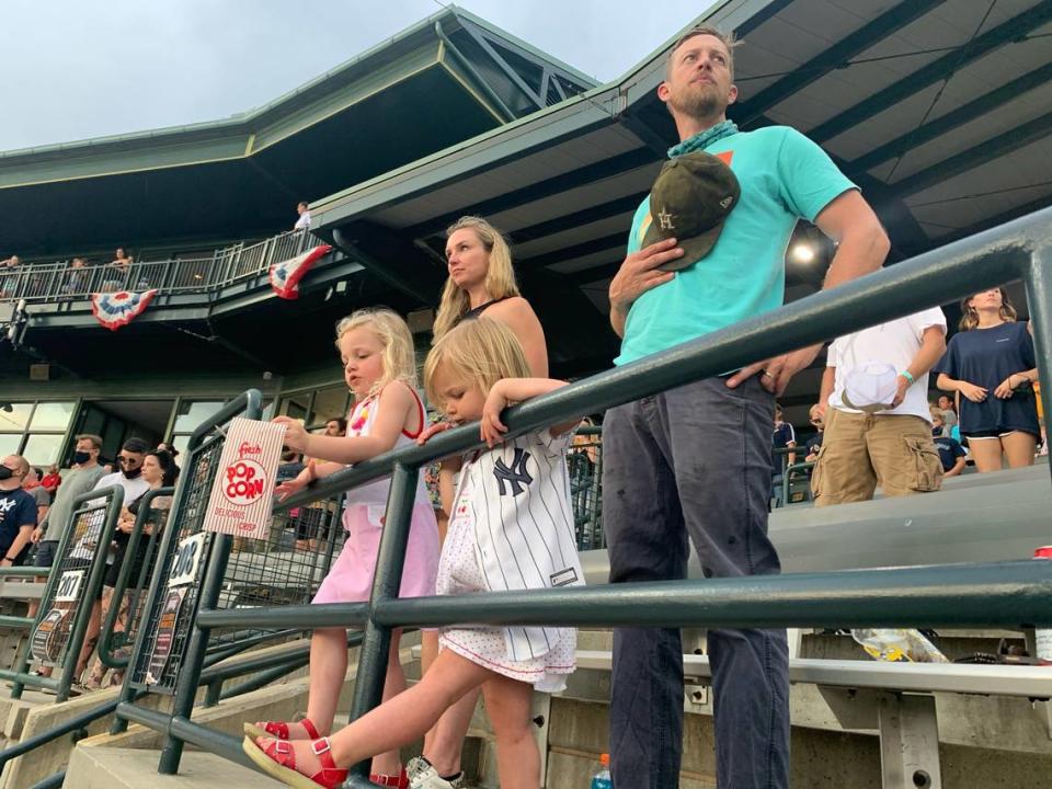 Kalee and Brock Smith stand for the national anthem as their girls, Kate, left, and Chandler, right, wait in matching shoes for the Charleston RiverDogs season opener to start on May 4, 2021.