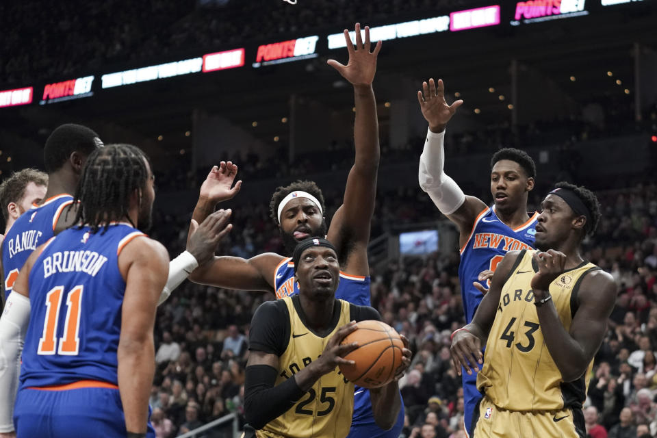 Toronto Raptors forward Chris Boucher (25) prepares to shoot while guarded by New York Knicks center Mitchell Robinson (23) and guard RJ Barrett (9) during first-half NBA basketball game action in Toronto, Friday, Dec. 1, 2023. (Arlyn McAdorey/The Canadian Press via AP)