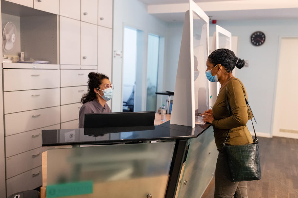 A person, wearing a face mask, talking to a receptionist, who's also wearing a face mask