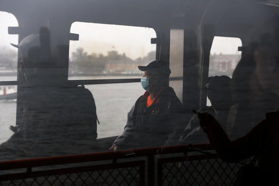 A man wearing a face mask, surrounded by a few others, looks out of a window at a body of water.