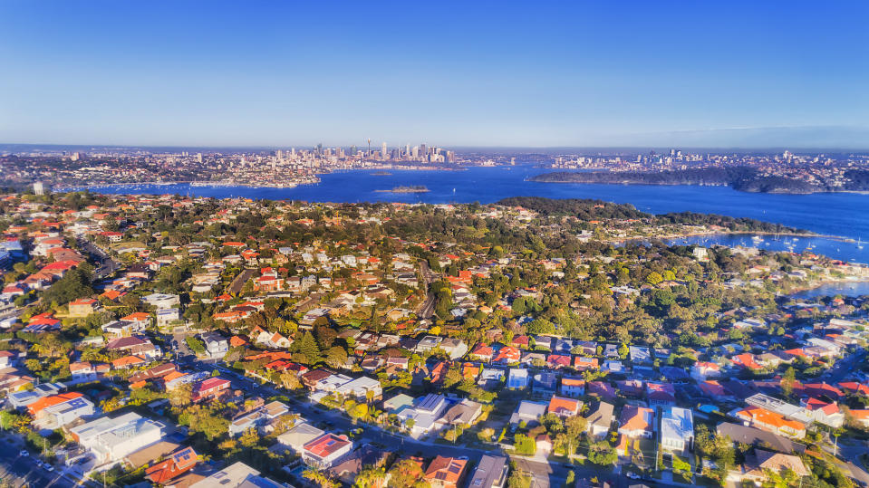 Eastern suburbs of Sydney in aerial view across Sydney harbour towards distant city CBD high-rise towers and waterfront under soft morning light on a bright clear day.