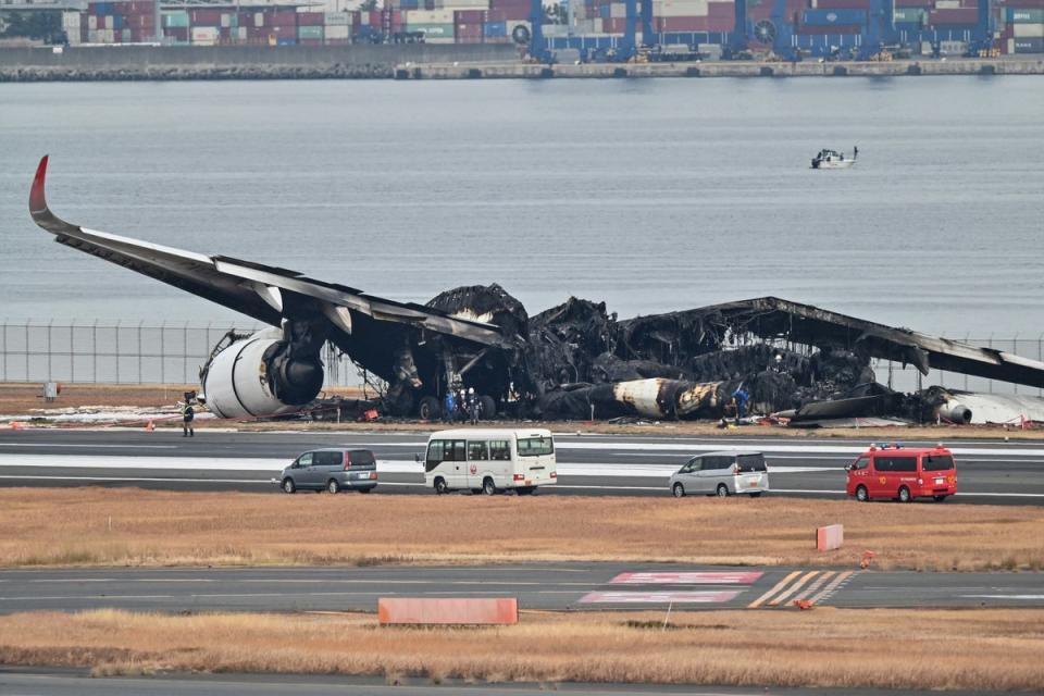 Officials look at the wreckage of the Japan Airlines plane on the tarmac (AFP via Getty Images)