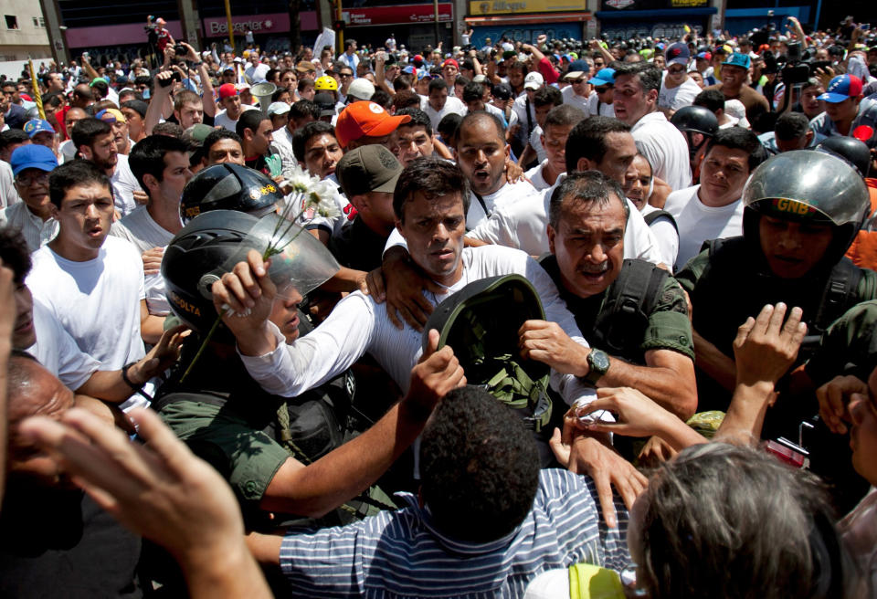 Opposition leader Leopoldo Lopez, dressed in white and holding up a flower stem, is taken into custody by Bolivarian National Guards, in Caracas, Venezuela, Tuesday, Feb 18, 2014. Lopez re-emerged from days of hiding to address an anti-government demonstration and then he turned himself in to authorities Tuesday. Speaking to some 5,000 supporters with a megaphone, Lopez said that he doesn't fear going to jail to defend his beliefs and constitutional right to peacefully protest against President Nicolas Maduro.(AP Photo/Alejandro Cegarra)