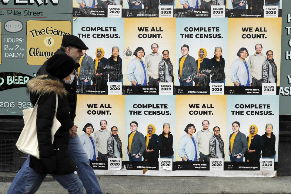 FILE - In this April 1, 2020, file photo, people walk past posters encouraging participation in the 2020 Census in Seattle's Capitol Hill neighborhood. The U.S. Census Bureau has spent much of the past year defending itself against allegations that its duties have been overtaken by politics. With a failed attempt by the Trump administration to add a citizenship question, the hiring of three political appointees with limited experience to top positions, a sped-up schedule and a directive from President Donald Trump to exclude undocumented residents from the process of redrawing congressional districts, the 2020 census has descended into a high-stakes partisan battle. (AP Photo/Ted S. Warren, File)