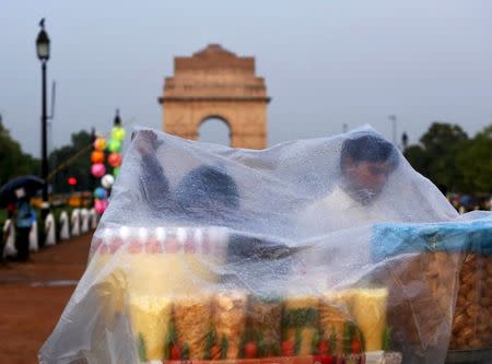 Roadside eatery hawkers use a plastic sheet to cover themselves from a rain shower in front of India Gate in New Delhi, June 23, 2015. REUTERS/Anindito Mukherjee/Files