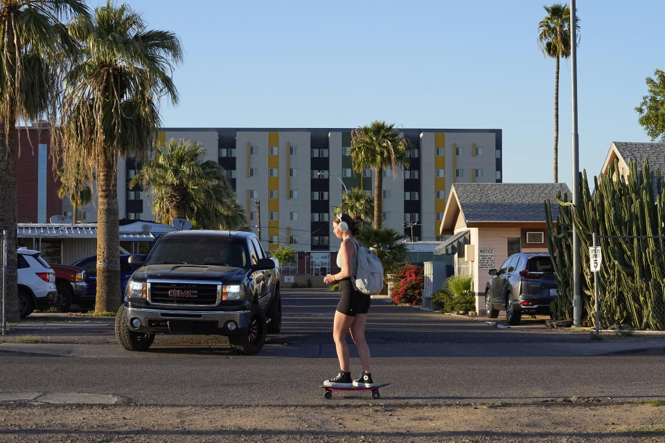 A student skateboards past the Periwinkle Mobile Home Park as student housing rises above the background, Thursday, April 11, 2023, in Phoenix. Residents of the park are facing an eviction deadline of May 28 due to a private university's plan to redevelop the land for student housing. (AP Photo/Matt York)