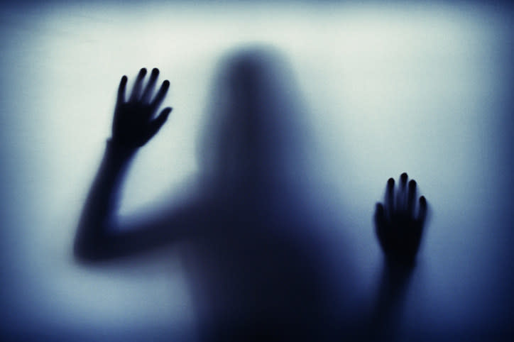 A blurry silhouette of a person with hands pressed against frosted glass. The figure appears to be in a state of tension or distress