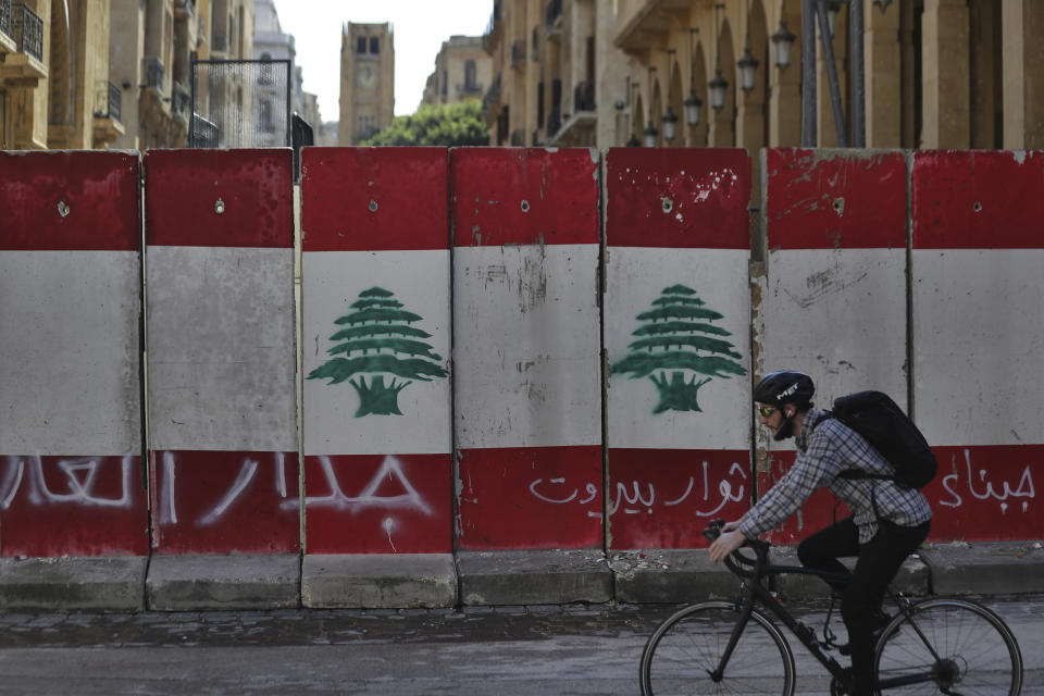 A man rides his bicycle next to a concrete wall installed by authorities to blocks a road leading to the parliament building, in downtown Beirut, Lebanon, Friday, Jan. 24, 2020. Arabic on the wall reads "wall of shame, left, Beirut rebels, center, Cowards." As cement barricades come up across the capital, blocking the path to major government buildings, Lebanese protesters vowed to continue taking to the street on the 100-day anniversary of the anti-government protests. (AP Photo/Hassan Ammar)