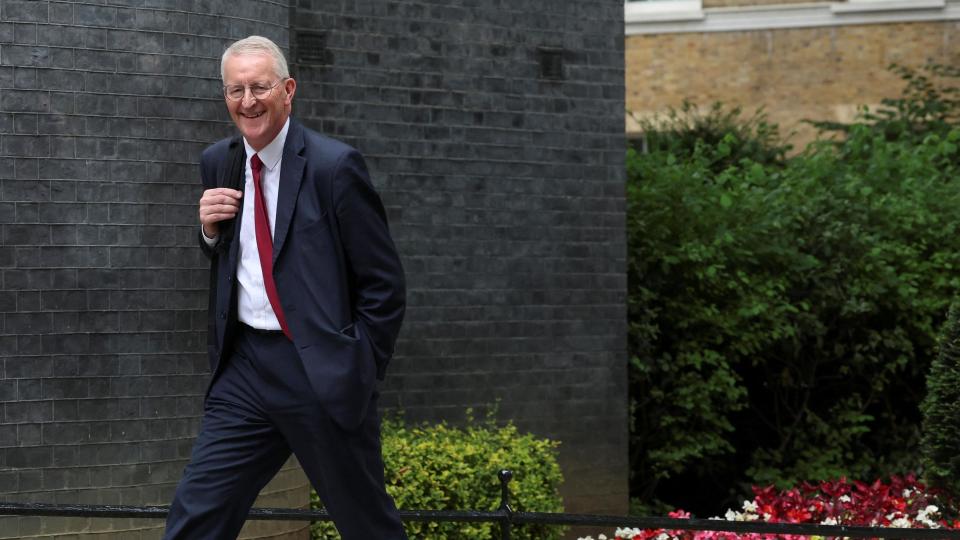 Hilary Benn walking into No 10 Downing Street. He has a smile on his face and he's wearing a suit and a red tie