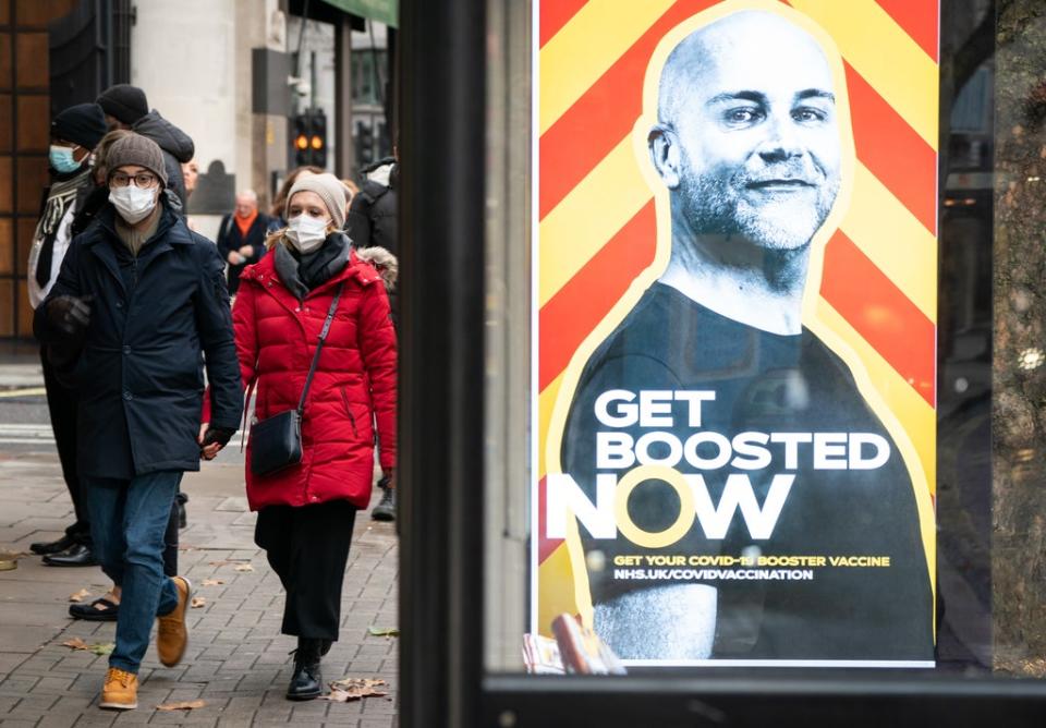People wearing face masks walk past a UK Government advert encouraging people to book Covid booster vaccinations (PA)