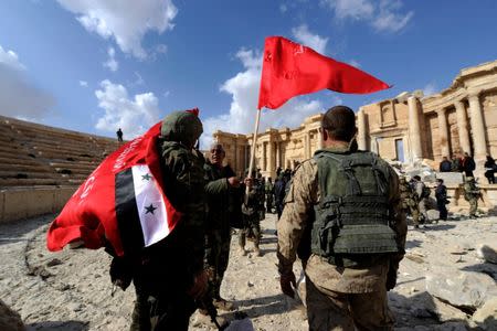 Syrian army soldiers carry flags in the amphitheater of the historic city of Palmyra, Syria March 4, 2017. REUTERS/Omar Sanadiki