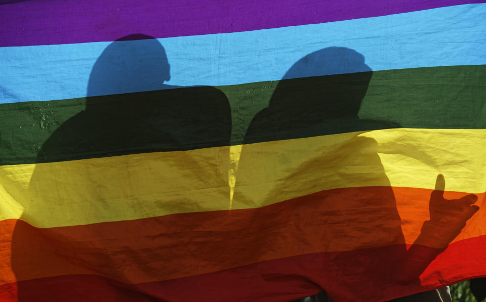 FILE - In this Friday, May 17, 2019 file photo, LGBT refugees living in Kenya stand behind a rainbow flag as they protest against their treatment by authorities, outside an office of the UN refugee agency UNHCR in Nairobi, Kenya. LGBT refugees allege they have been harassed by police in recent weeks in Kenya, which is a rare regional haven for the gay community yet maintains that gay sex is illegal. (AP Photo/Ben Curtis, File)