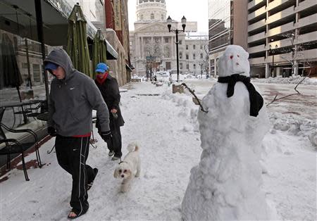 A couple walks their dog past a snowman near the State Capitol building in Indianapolis, Indiana January 6, 2014. REUTERS/Nate Chute