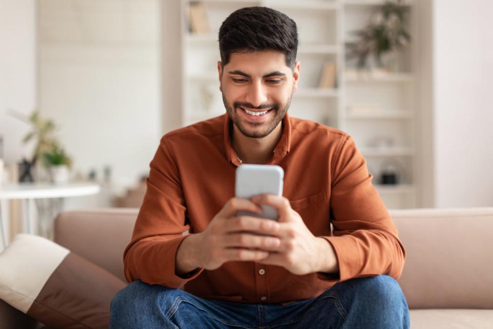 An investor, seated on a couch in a living room, smiles while looking at a phone.