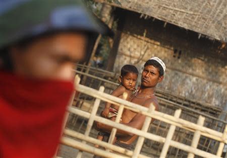 A Rohingya man carrying his child looks at police and volunteer conducting a national census at a Rohingya village in Sittwe, the capital of Rakhine State April 1, 2014. REUTERS/Soe Zeya Tun