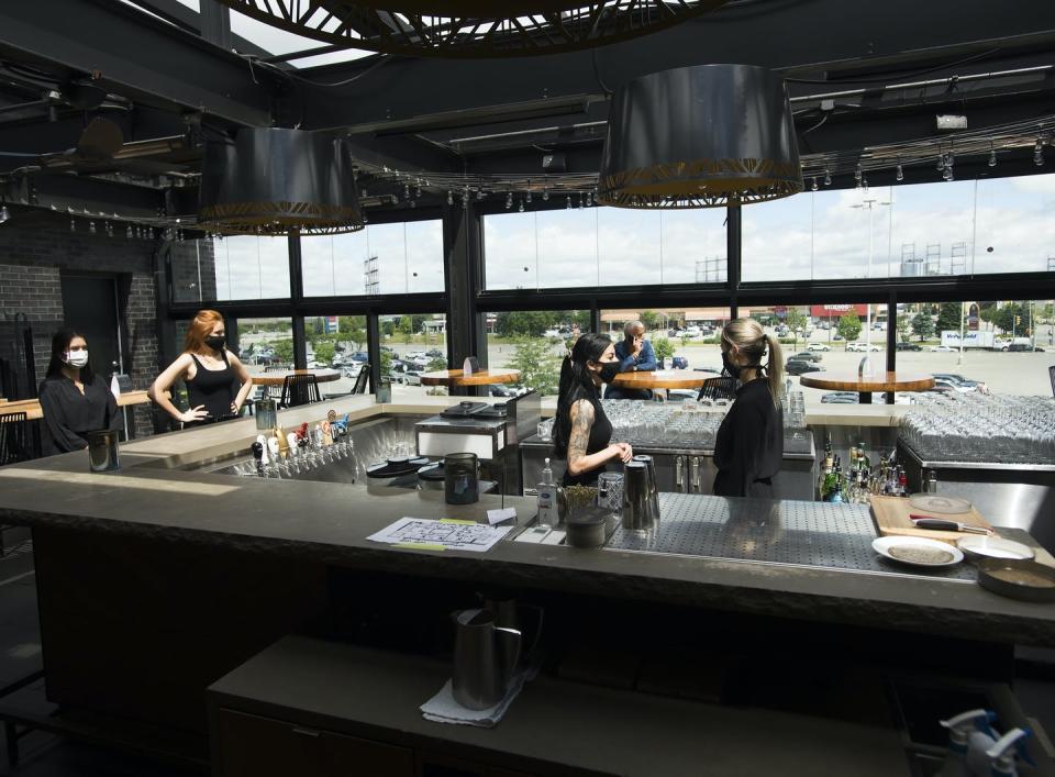 Bartenders and wait staff, all wearing masks, inside a restaurant.