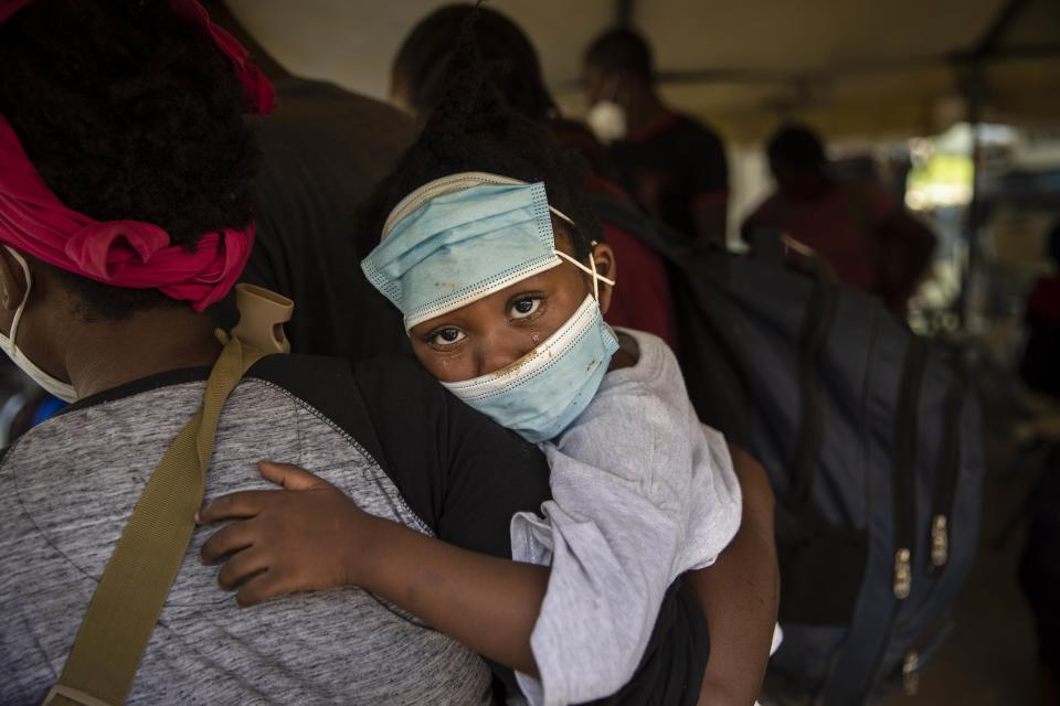 A little girl with teary eyes holds is carried by a woman who was deported from the U.S. border with Mexico at Toussaint Louverture International Airport in Port-au-Prince, Haiti, Monday, Sept. 20, 2021. The U.S. is flying Haitians camped in a Texas border town back to their homeland. (AP Photo/Rodrigo Abd)