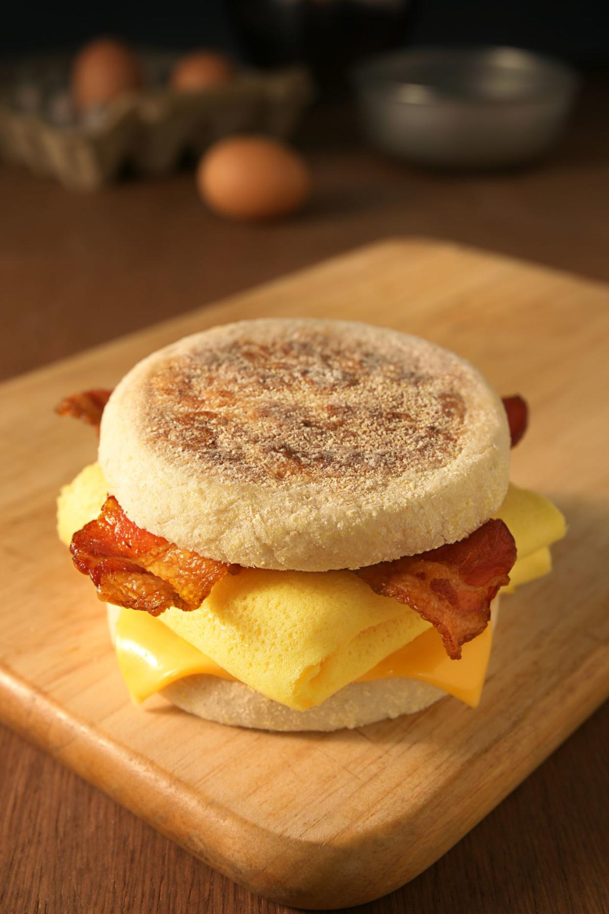 Focus on an egg sandwich on a wooden cutting board on a wooden table with eggs blurred in the background